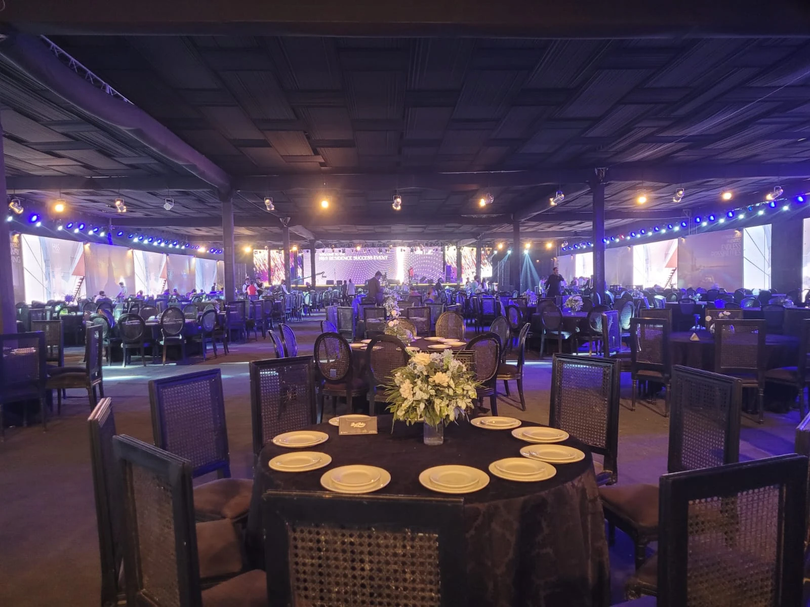 Round tables prepared for an evening event under decorative lighting.