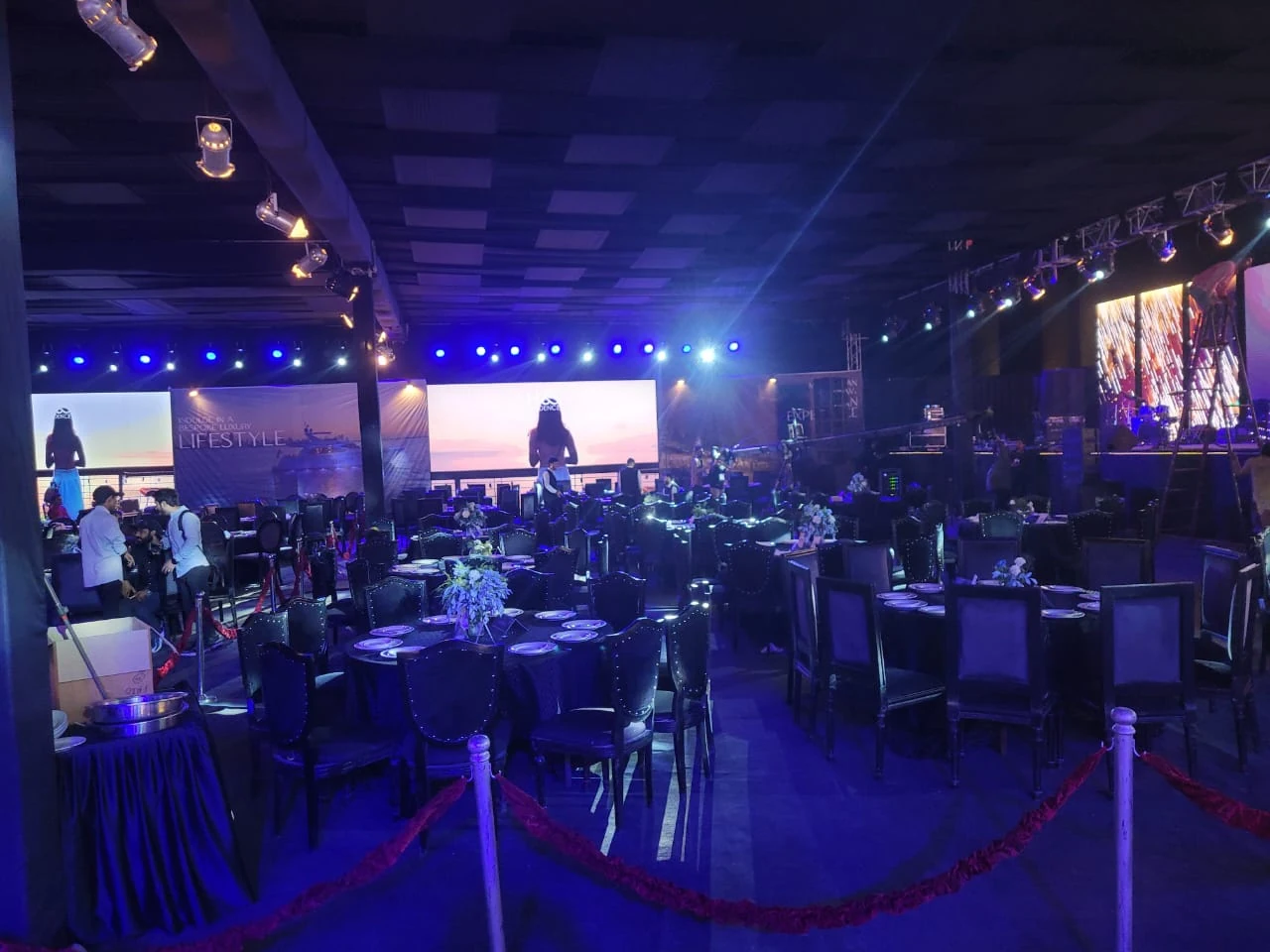 An evening event space with tables, a stage and blue lighting.